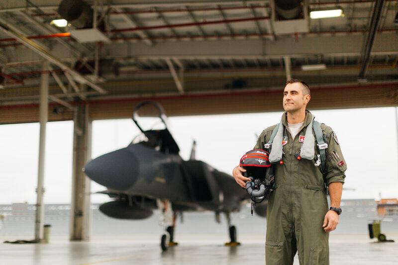 A pilot poses in front of an F-15 at Barnes Air National Guard Base wearing a flight suit for these F-15 fighter pilot family photos