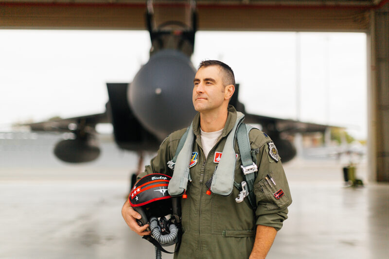 A pilot poses in front of an F-15at Barnes Air National Guard Base wearing a flight suit for these F-15 fighter pilot family photos