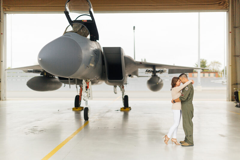 A pilot and his wife stand together in front an F-15 at Barnes Air National Guard Base wearing a flight suit and a coordinated outfit for these F-15 fighter pilot family photos