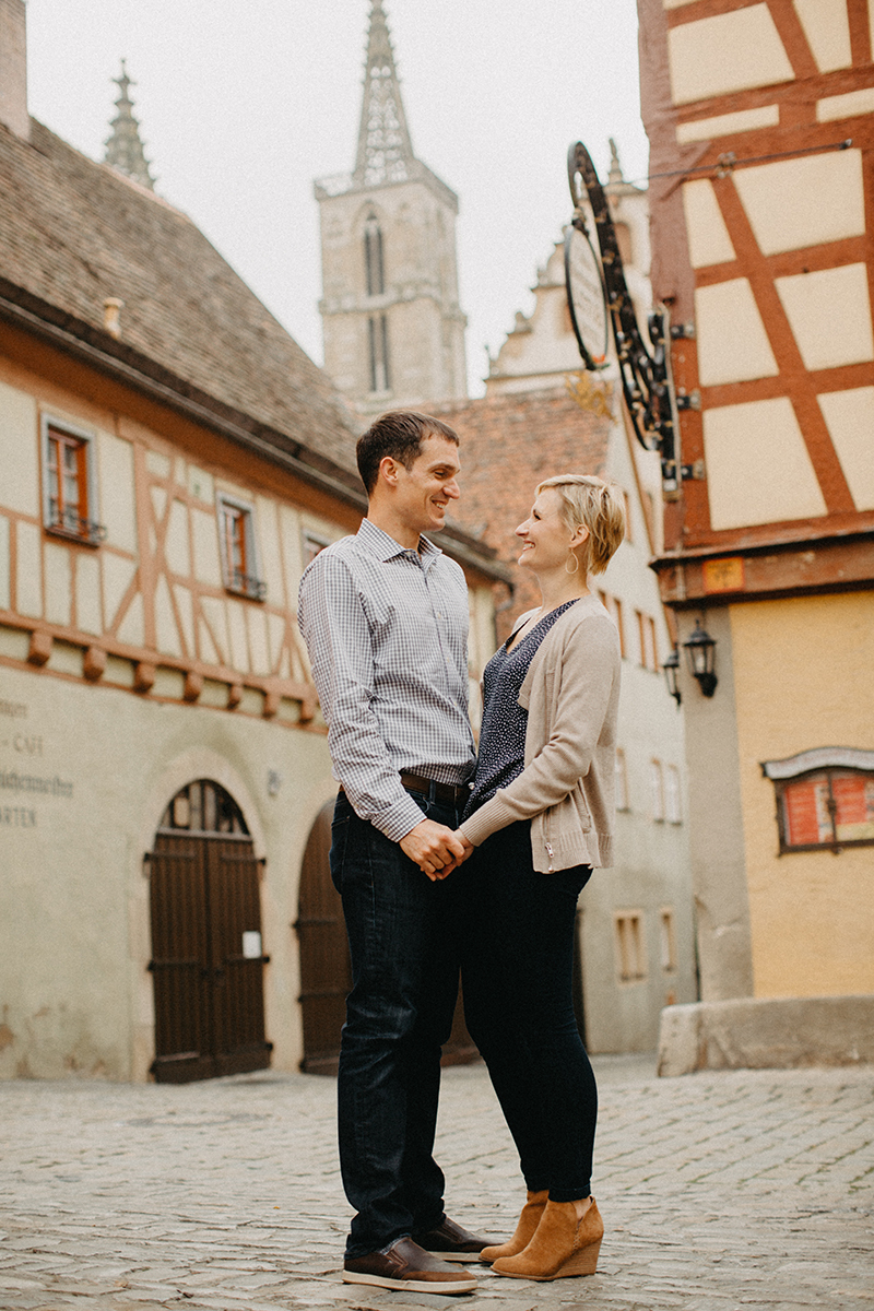 A couple hold hands and smile at one another in Germany wearing coordinated outfits for a Rothenburg ob der Tauber family photography session