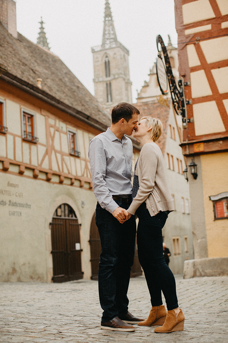 A couple hold hands and kiss in Germany wearing coordinated outfits for a Rothenburg ob der Tauber family photography session