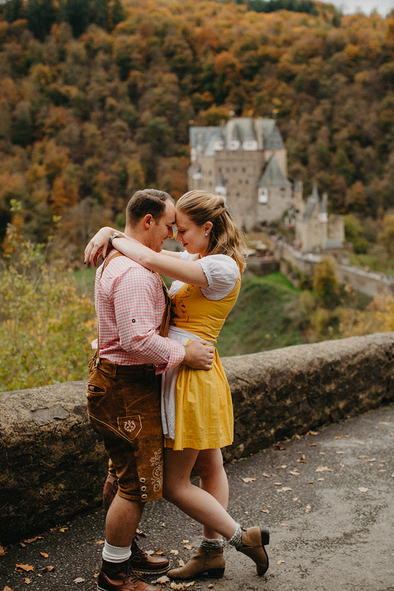 A couple hold one another on the road to Burg Eltz wearing a traditional dirndl and lederhosen for these Eltz Castle couples photos in Germany
