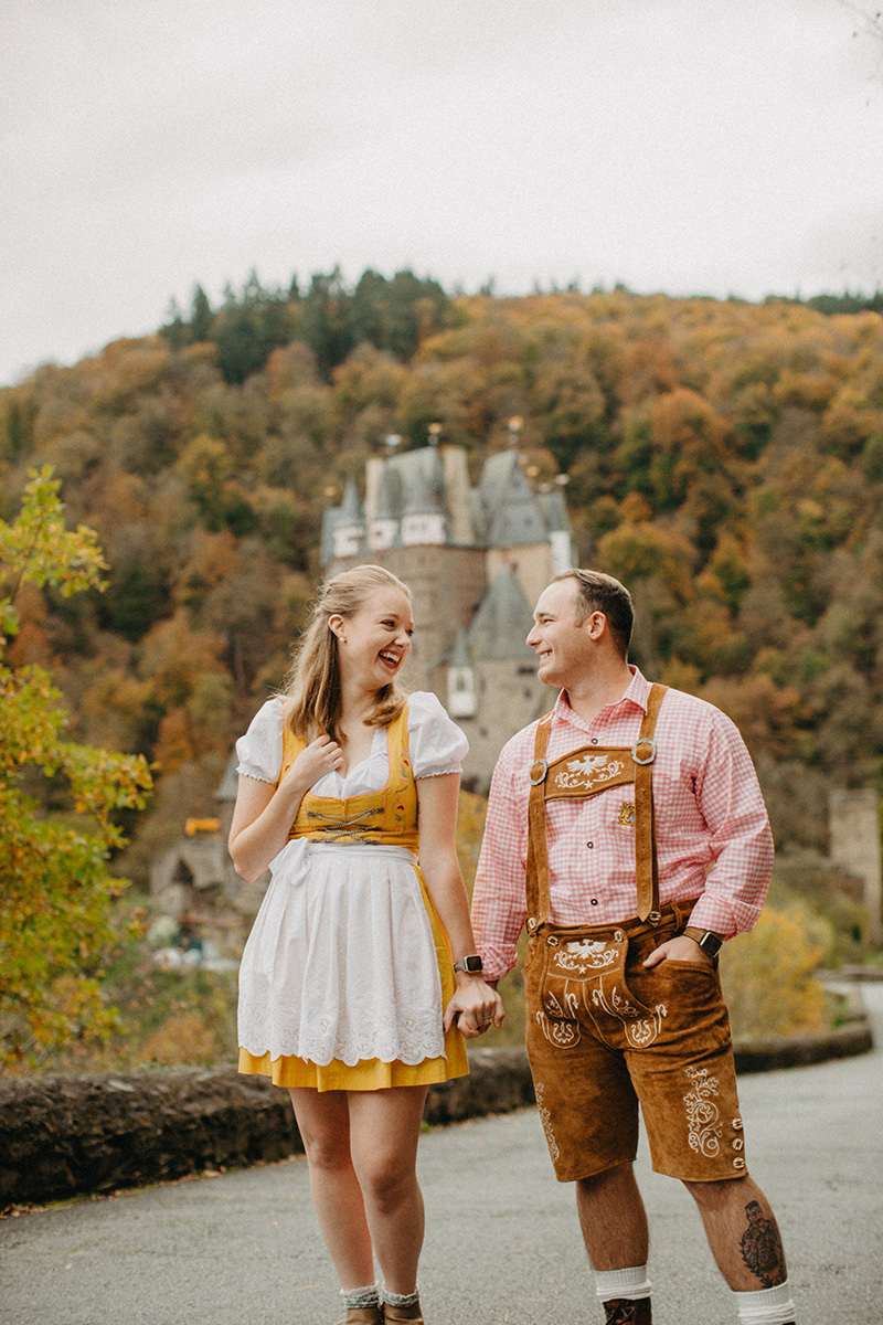 A couple hold hands on the road to Burg Eltz wearing a traditional dirndl and lederhosen for these Eltz Castle couples photos in Germany