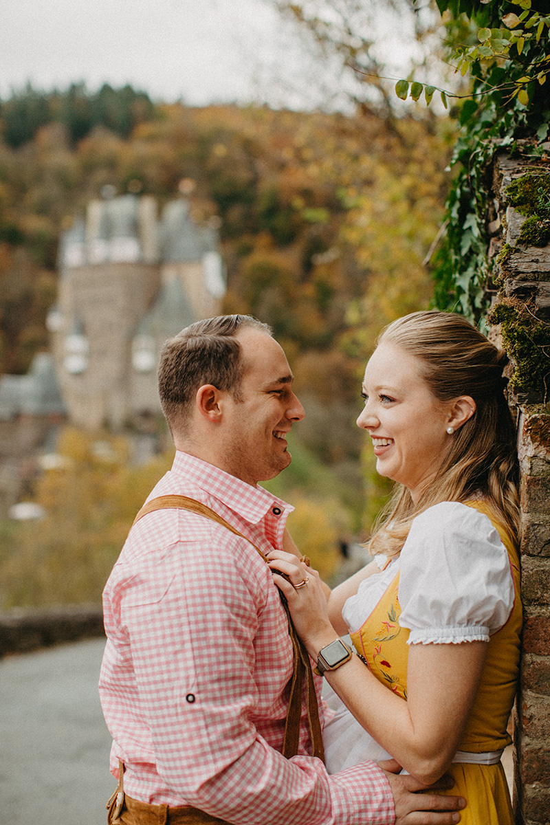 A couple embrace on the road to Burg Eltz wearing a traditional dirndl and lederhosen for these Eltz Castle couples photos in Germany