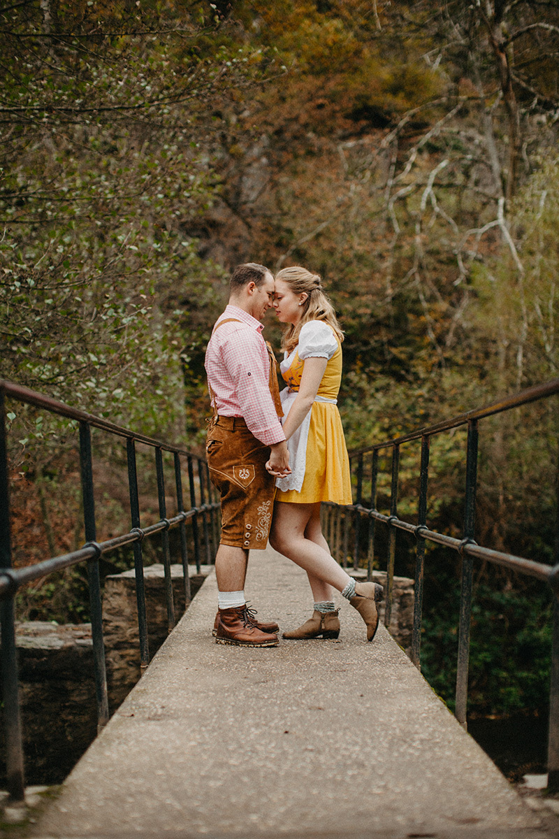 A couple embraces on a bridge near Burg Eltz wearing a traditional dirndl and lederhosen for these Eltz Castle couples photos in Germany