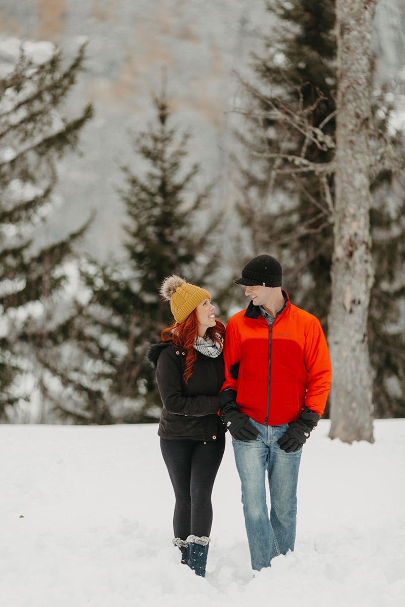 A couple walks together in trees on a snow covered mountain in Switzerland wearing snow gear for a Mürren couples photography session