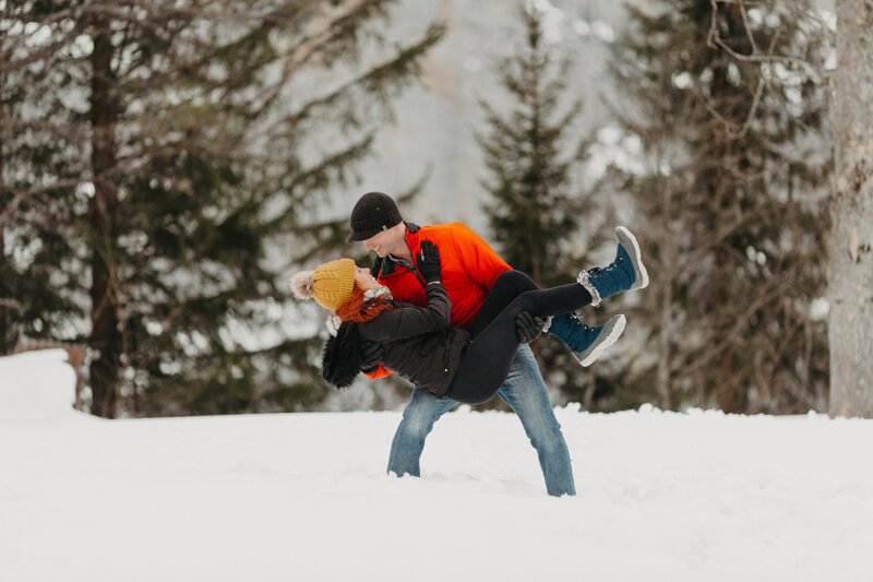 A couple embraces in trees on a snow covered mountain in Switzerland wearing snow gear for a Mürren couples photography session