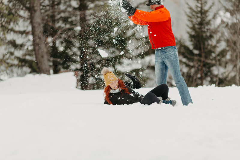 A couple having a snowball fight in trees on a snow covered mountain in Switzerland wearing snow gear for a Mürren couples photography session
