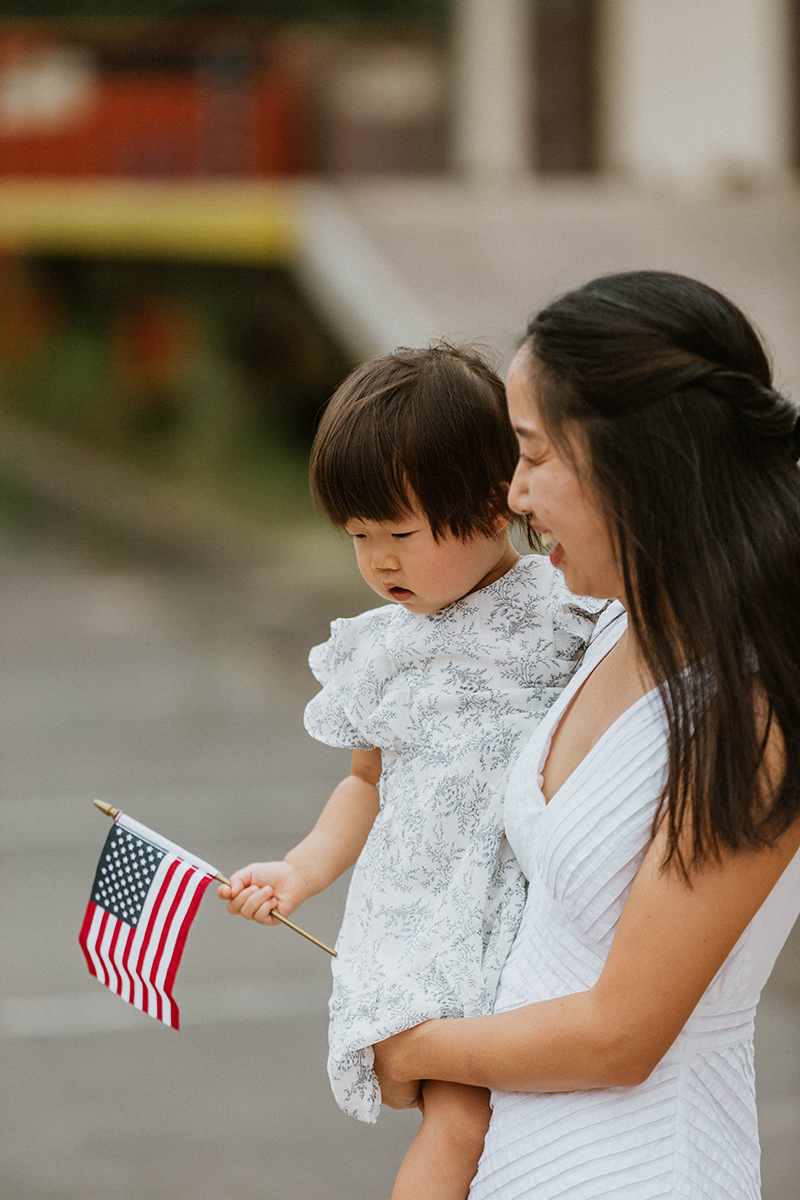 A woman holds her daughter with an American flag waiting at the Rhineland Ordnance Barracks for Kaiserslautern homecoming photos in Germany